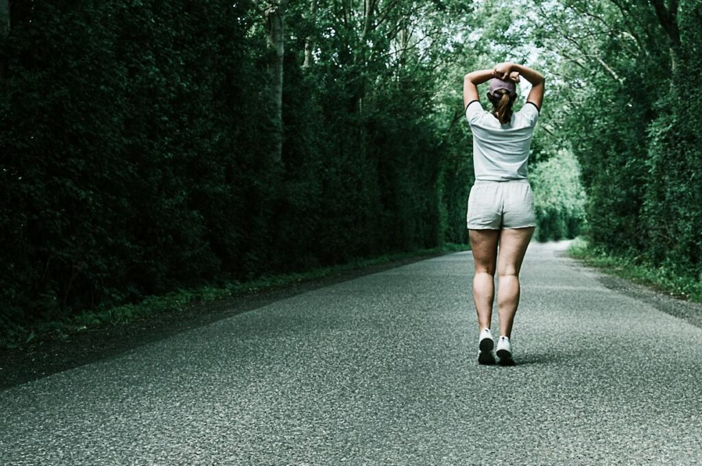 A woman jogs down a tree-lined road, embodying fitness and nature in a serene summer setting.